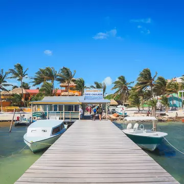 Boats line a colorful beachside pier in Belize on a sunny day. 