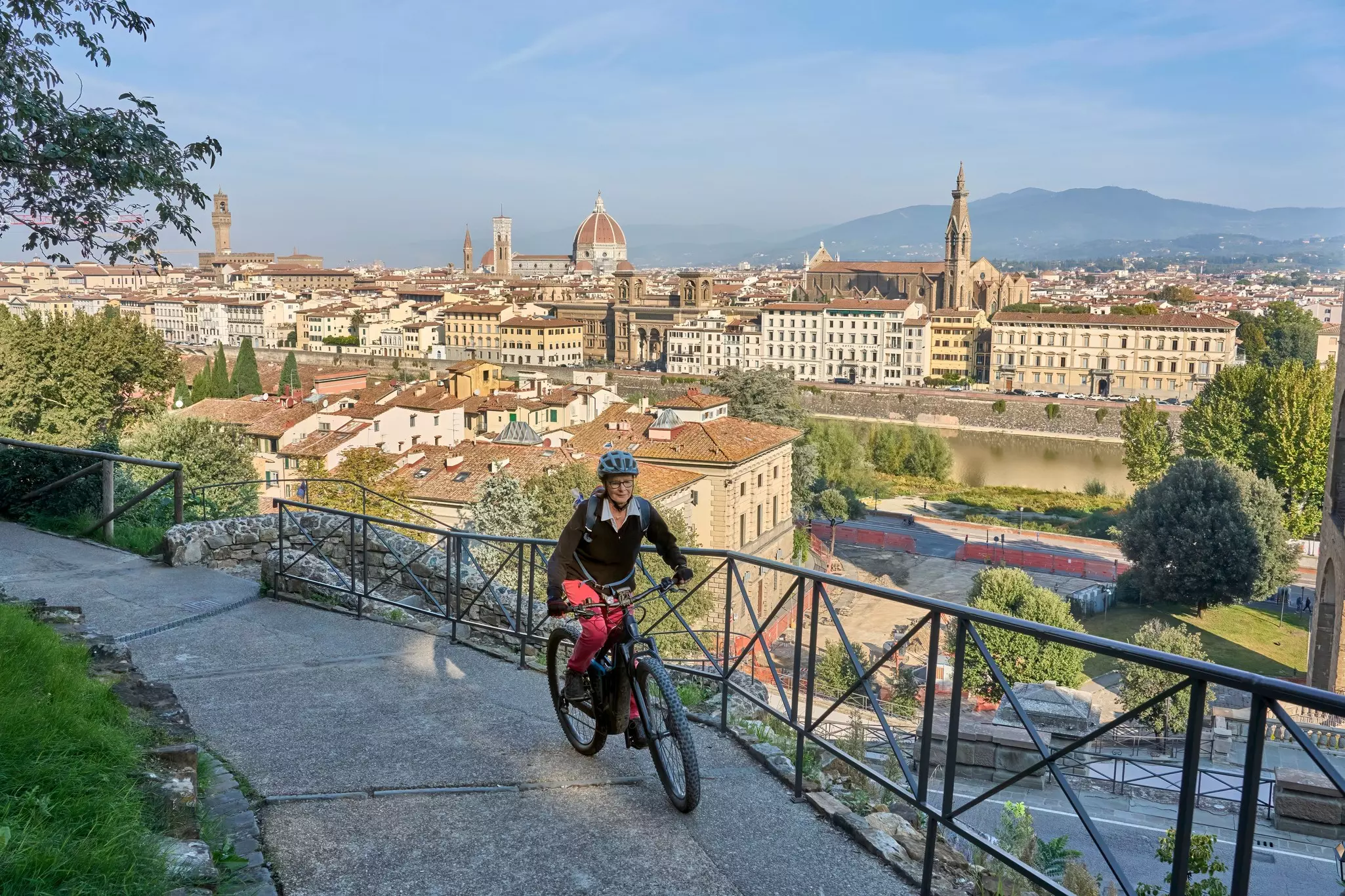 An older woman on an e-bike makes her way on a path above the historic center of Florence, Italy