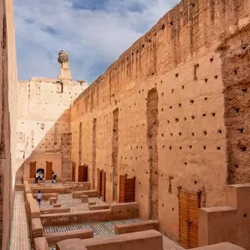 High ochre walls pocked with holes above tiled floor remnants and wooden doors, a large nest on a pillar top