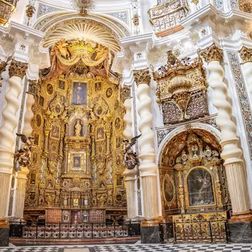 The interior of a church reveals a lavish gilded altarpiece surrounded by spiral-patterned columns.