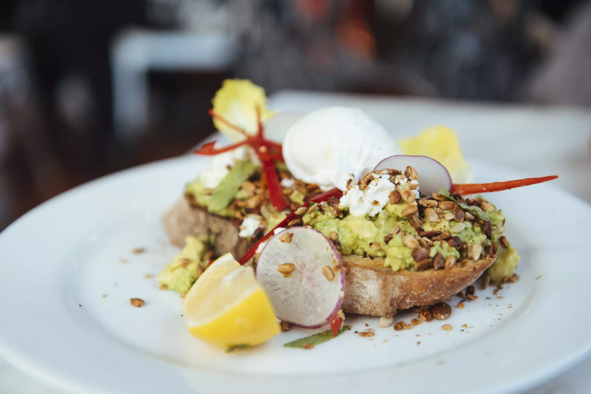 Sourdough bread with mashed avocados, poached egg, lemon, radish and seeds.