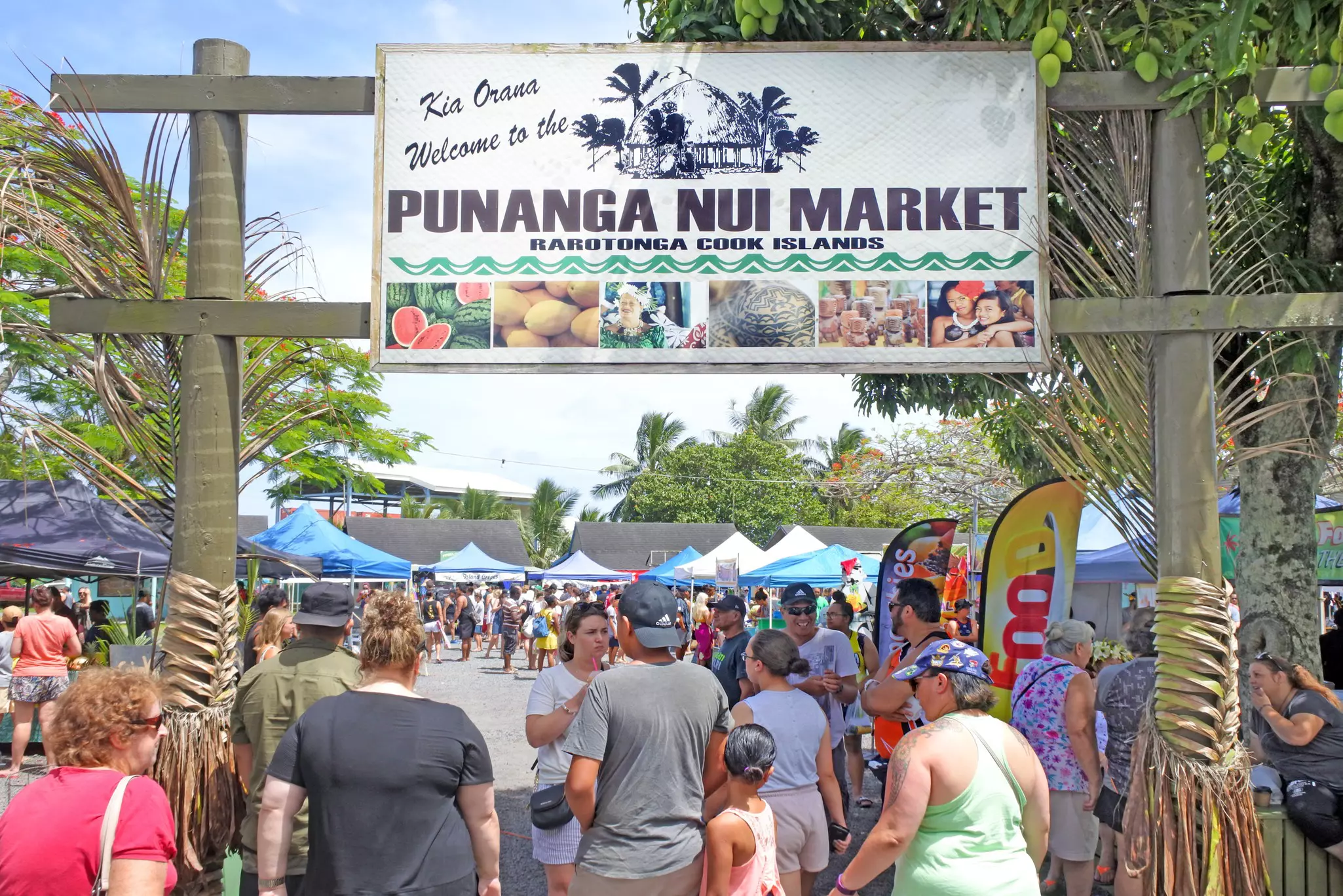 People enter a marketplace below a large sign that says "Welcome to Punanga Nui market"