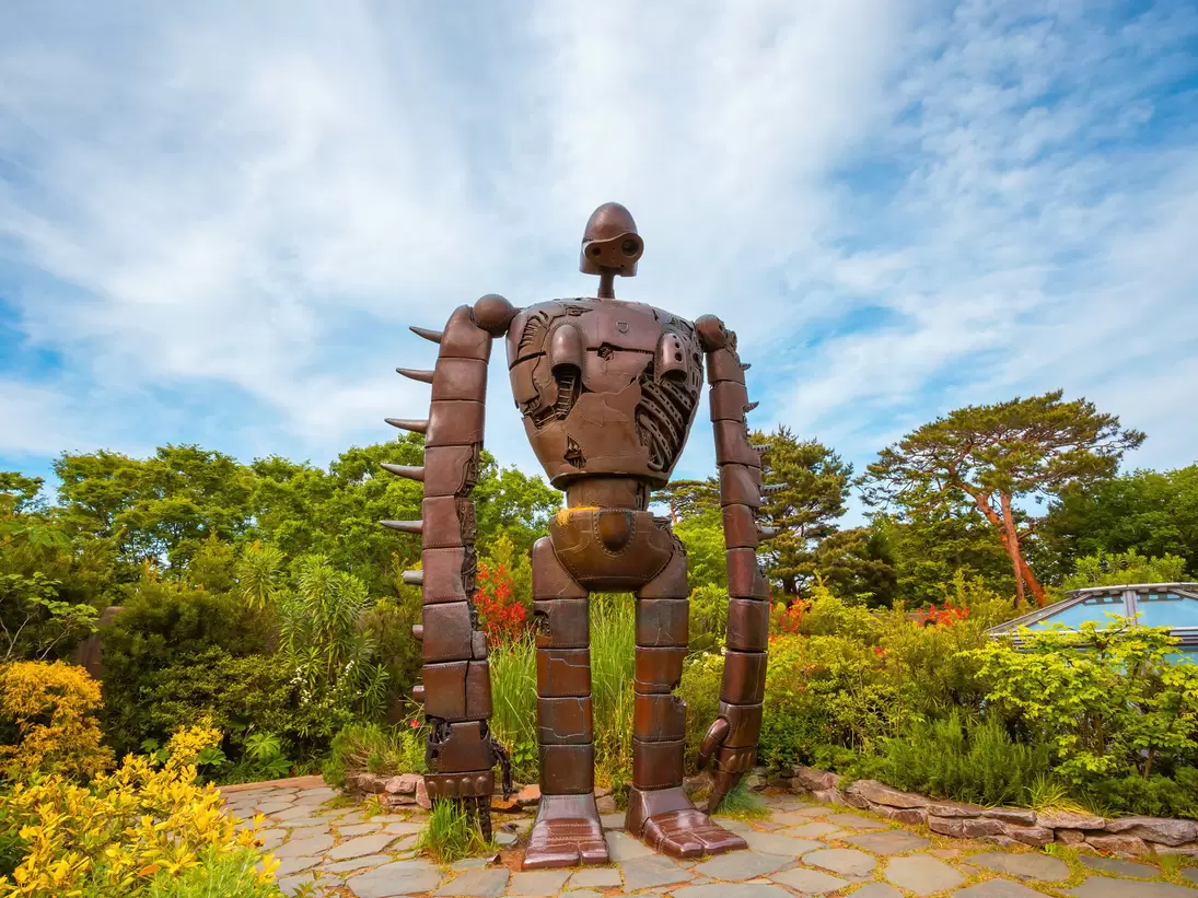 A large sculpture of a robot stands in a garden.