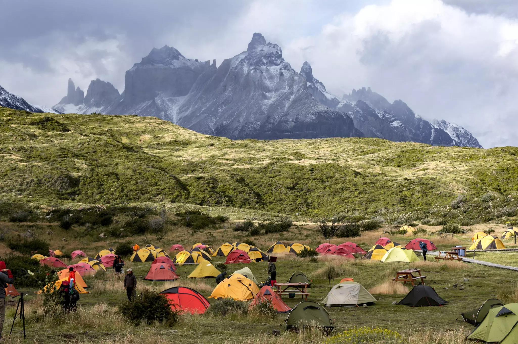 Red and yellow tents pitched in grass, with jagged peaks in the background.