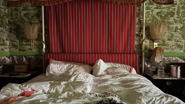 A rumpled bed of white sheets with red-and-white-striped headboard.