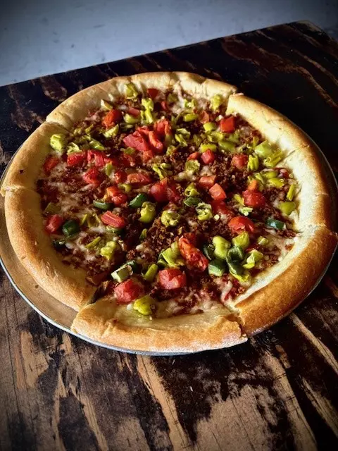 A pizza pie with meat and vegetables on a tin plate resting on a wooden table