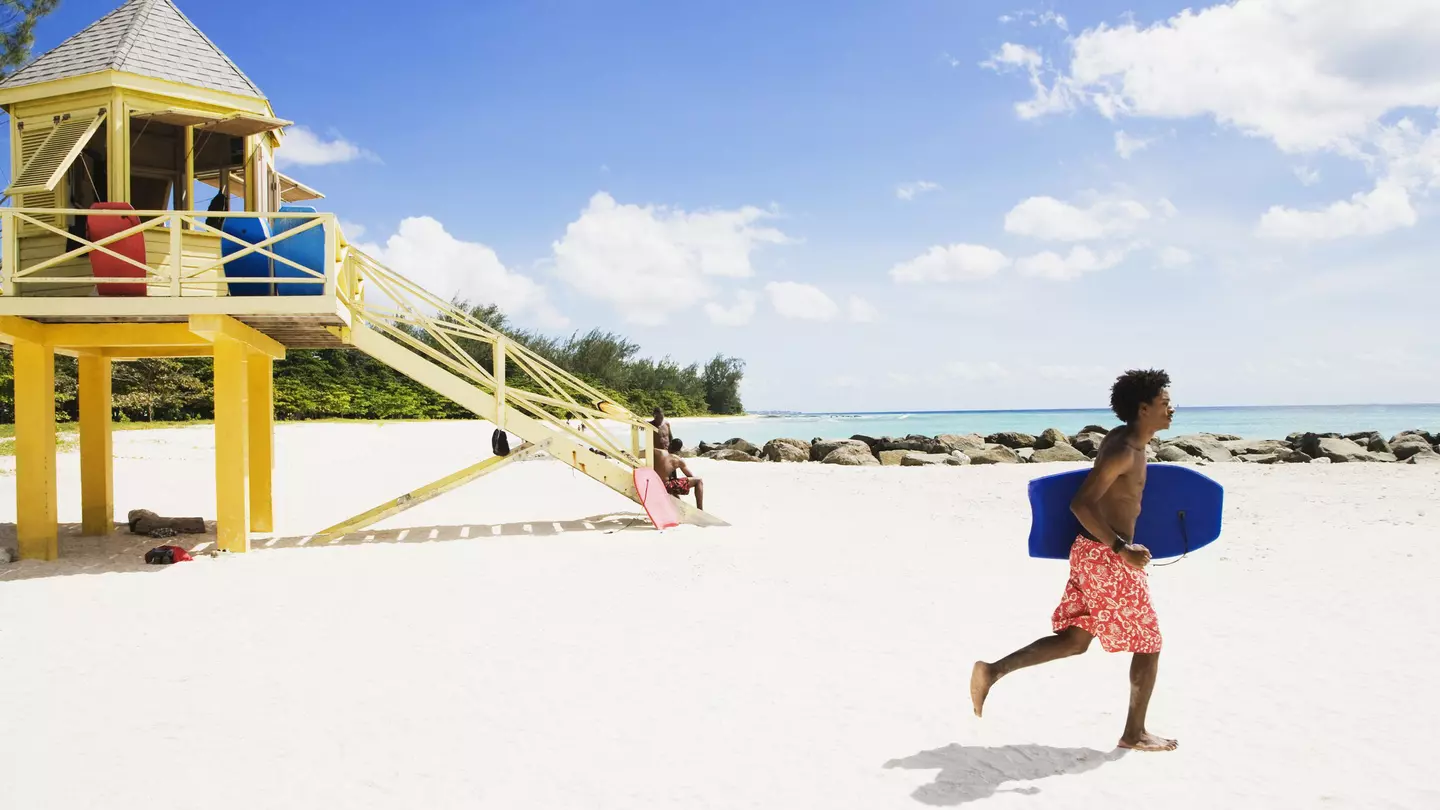 A bodyboarder runs along a beach in Barbados in front of a lifeguard tower