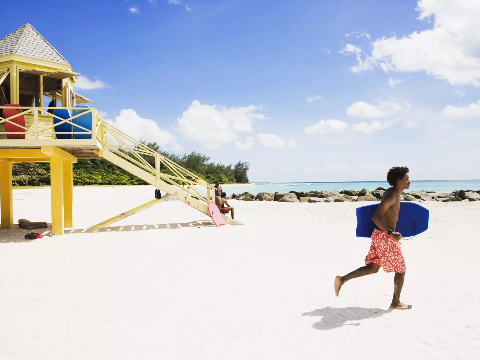A bodyboarder runs along a beach in Barbados in front of a lifeguard tower