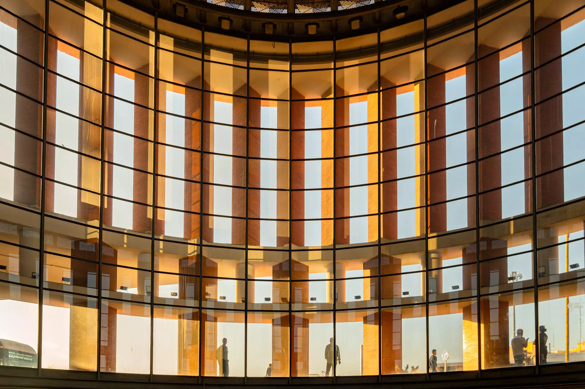 People standing in a glassed walkway below a grid of windows and columns at a train station in Madrid.