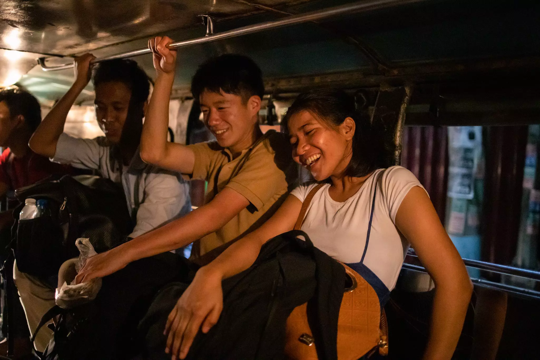 Young people smile in the back of a public open-air bus by night