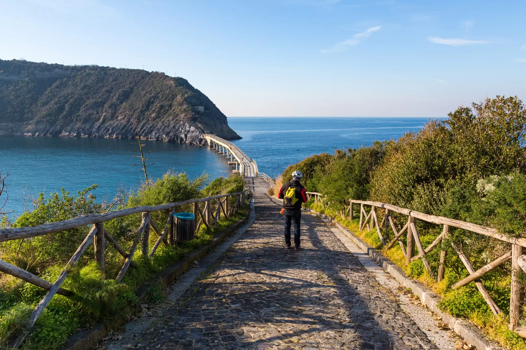 A man wearing a cycling helmet approaches the foot bridge that leads to Vivara Island, a nature reserve and protected oasis in Procida.