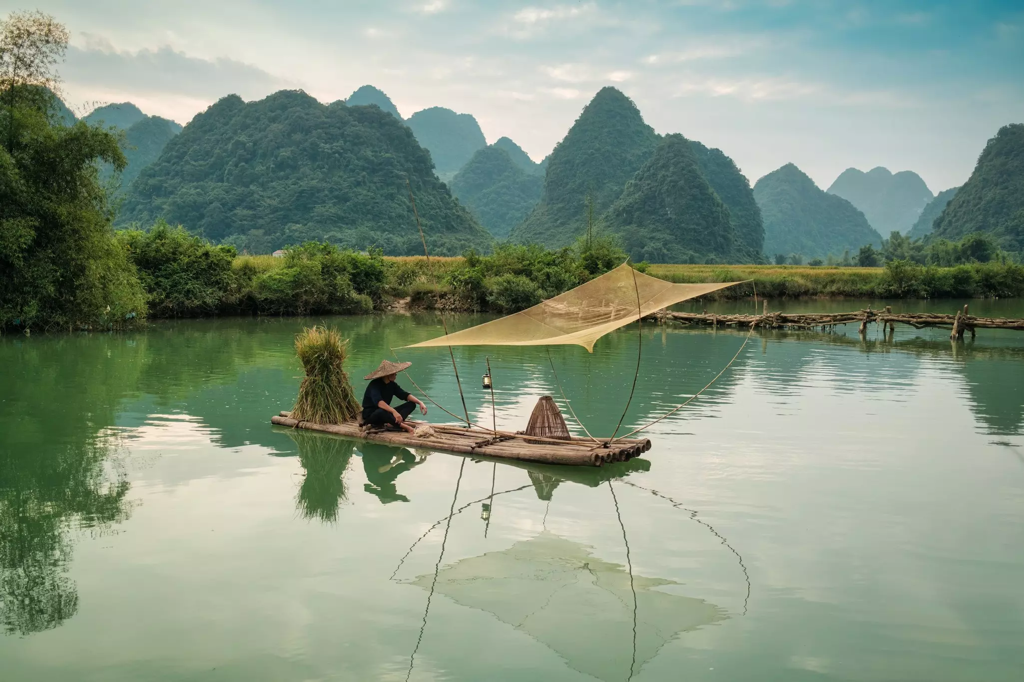 Fisherman with traditional fishing on wooden raft over the river in sunny day, Surrounded by mountain in Phong Nam Valley, Cao Bang, Vietnam,