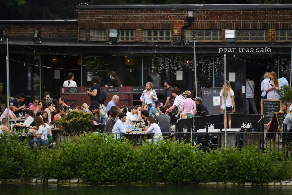 People sit outside a pub with "Pear Tree Cafe" on its black awning enjoying the warm weather.