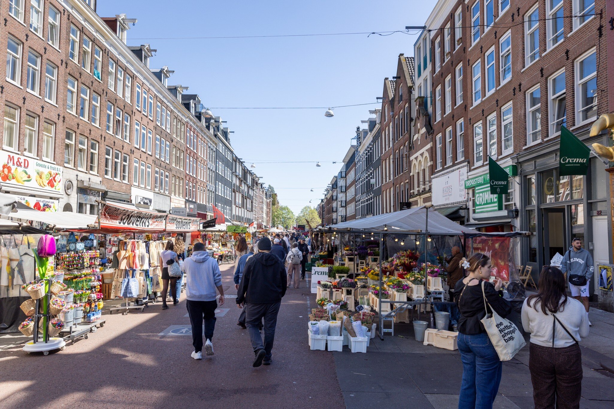 People walking at the bustling Albert Cuypmarkt on a sunny day in Amsterdam.