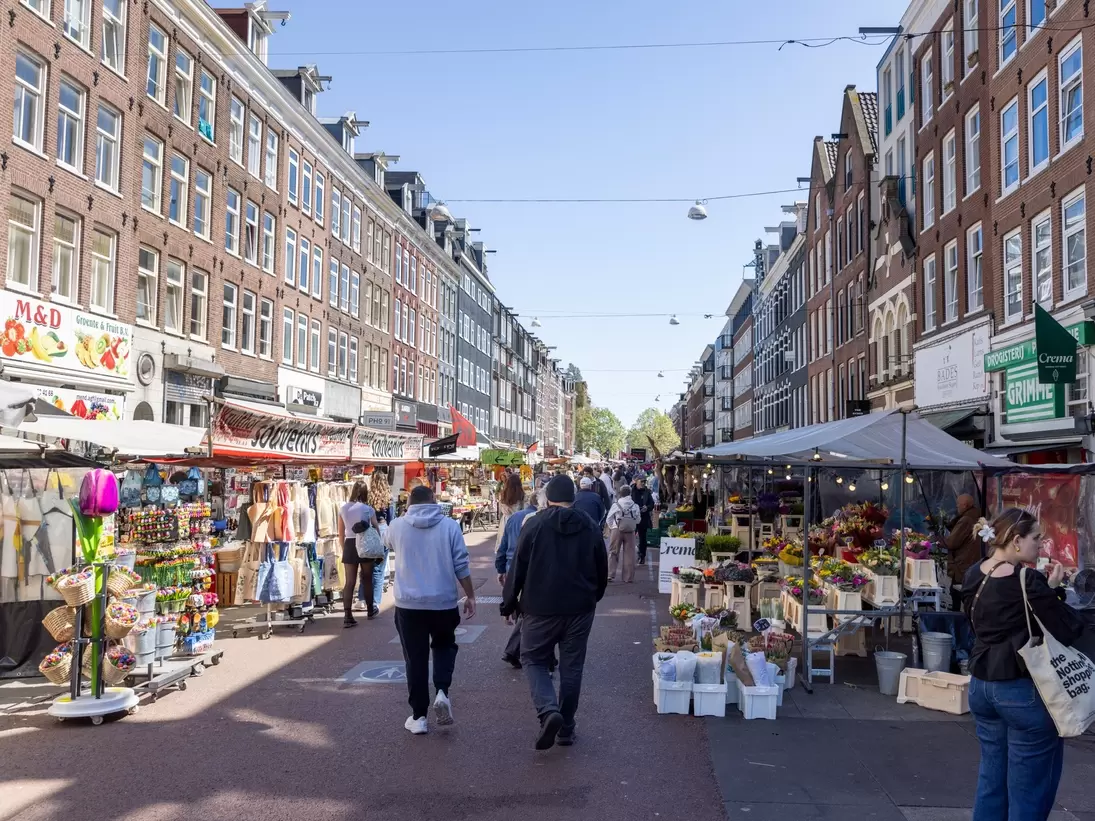 People walking at the bustling Albert Cuypmarkt on a sunny day in Amsterdam.