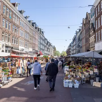 People walking at the bustling Albert Cuypmarkt on a sunny day in Amsterdam.