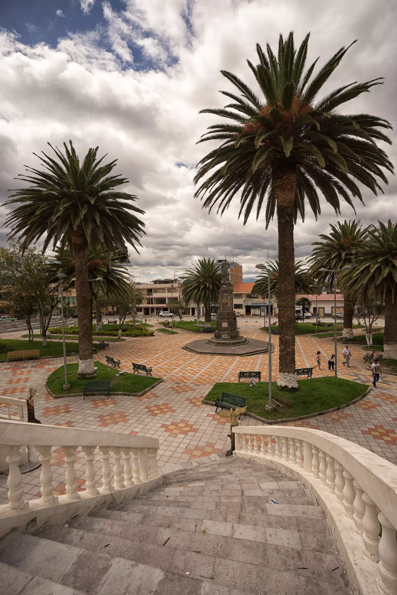 An ornate square with large trees and a few people wandering around in San Antonio, Ecuador. 