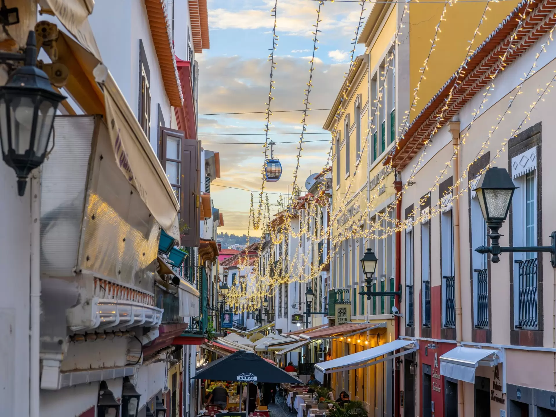 A gondola passes over a narrow pedestrian street with colorful buildings
