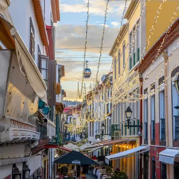 A gondola passes over a narrow pedestrian street with colorful buildings