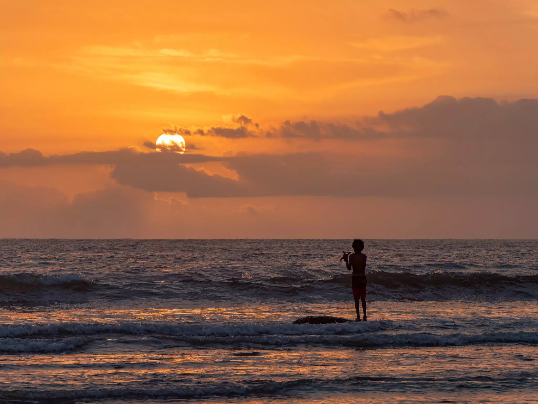 A fisher on a beach at sunset as waves roll up on the shore
