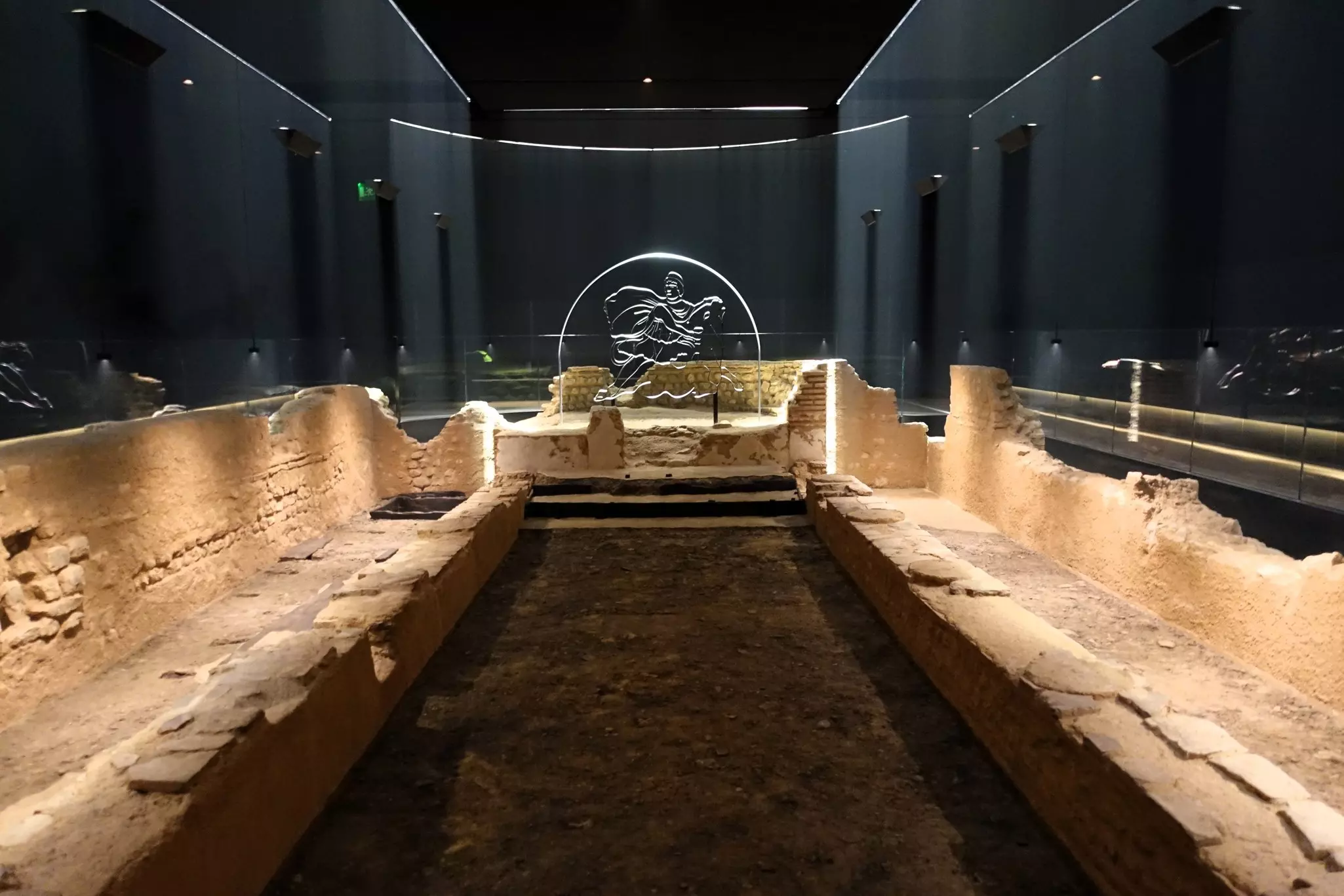 An employee poses alongside a reconstruction of the Roman Temple of Mithras. It is dark but the stone is illuminated by warm light.