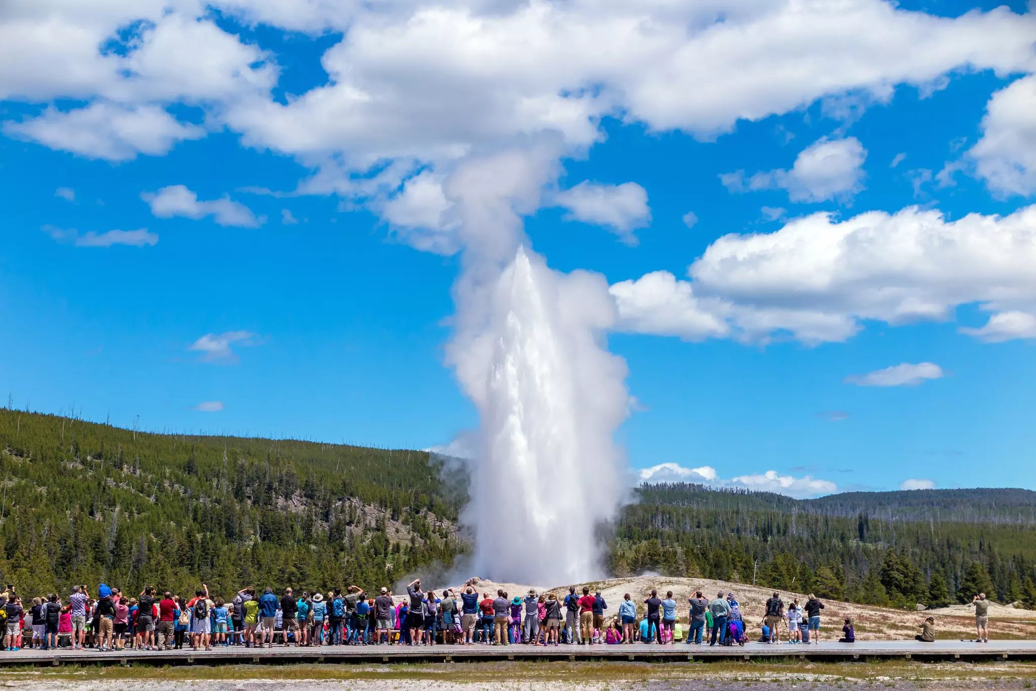 Tourists lined up along a boardwalk look towards a large jet of water that's shooting into the air
