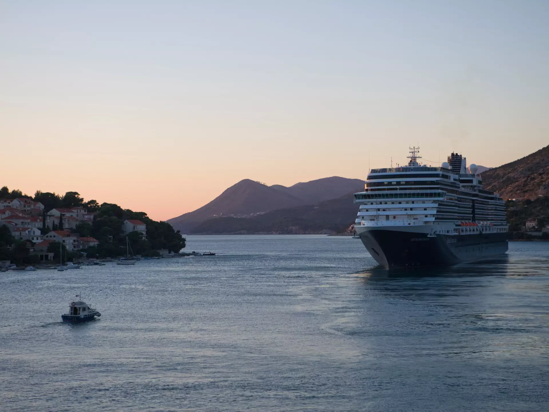 A cruise ship sails from a port at dusk