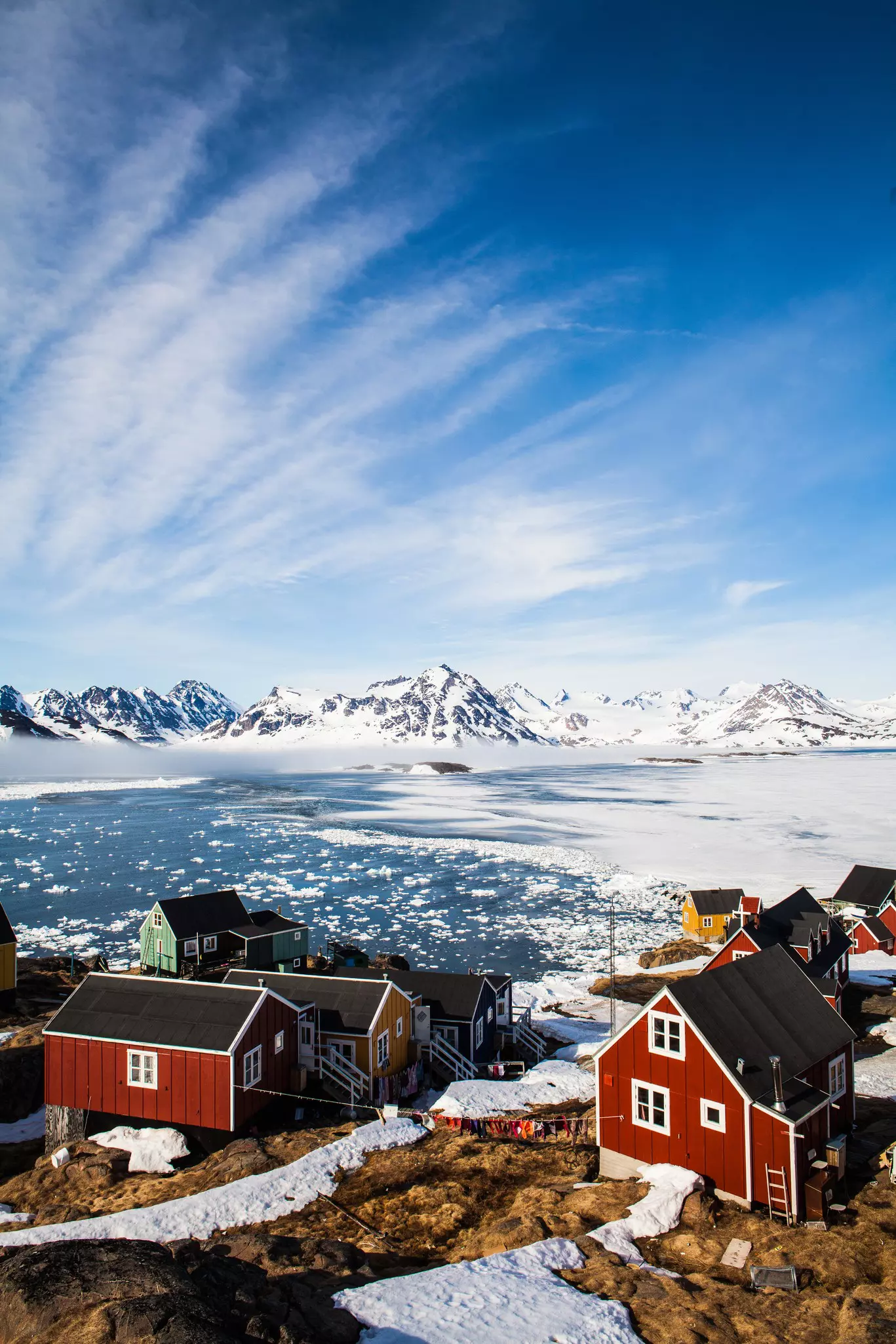 Small homes off the shore of icy waters and snow coated hills