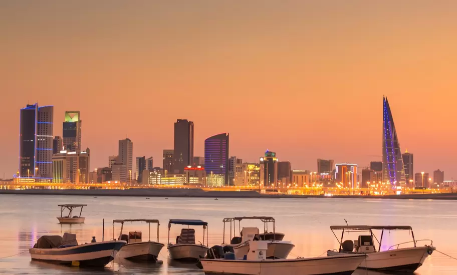 Manama skyline in Bahrain at dusk, including the sail-shaped Bahrain World Trade Center, with small boats on the shore