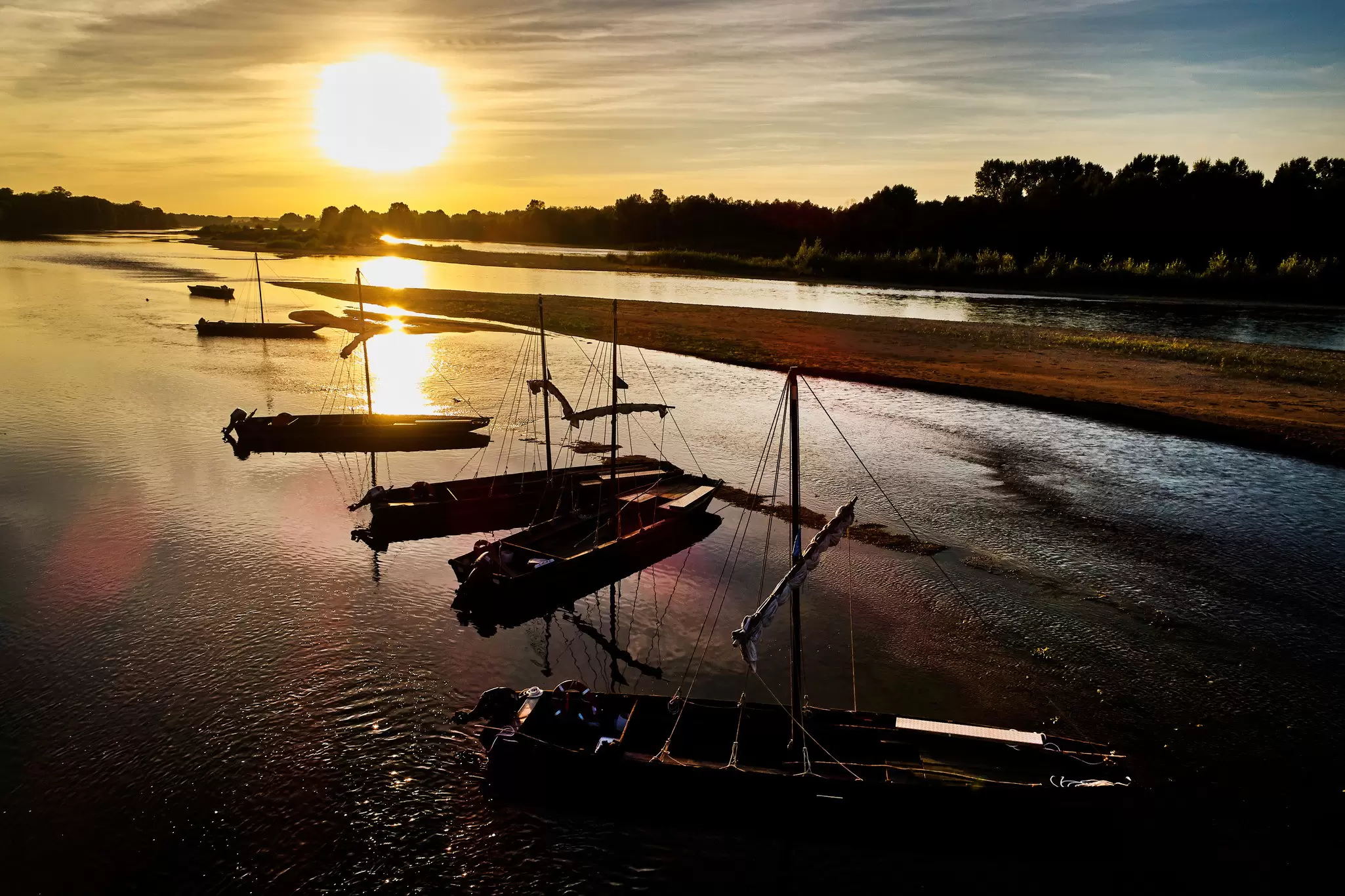 Flat-bottomed fishing boats are moored in a shallow section of a river, pictured at sunset.