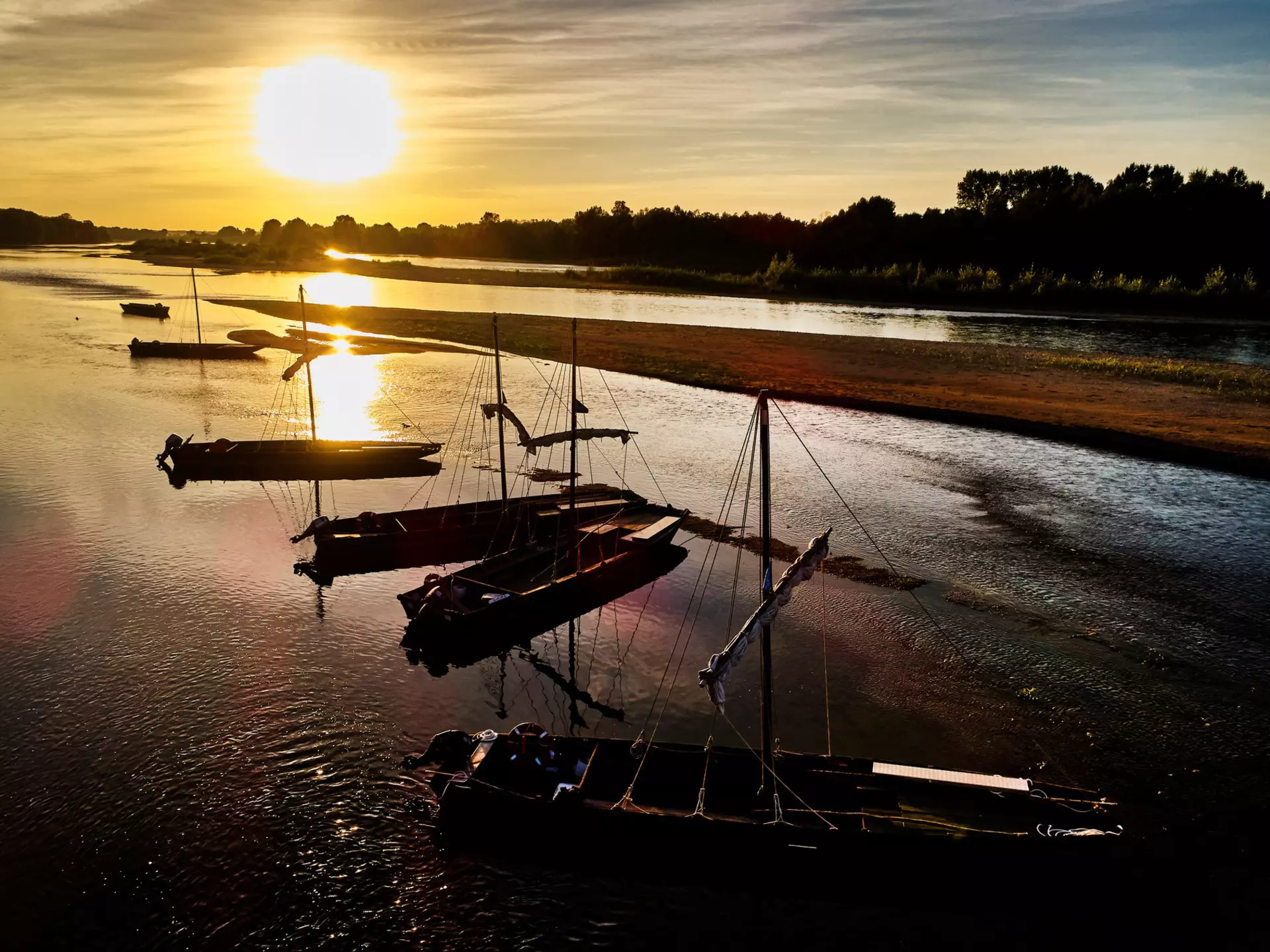 Flat-bottomed fishing boats are moored in a shallow section of a river, pictured at sunset.