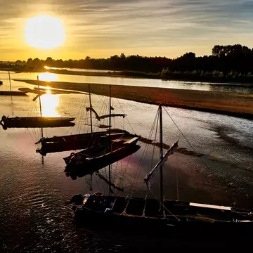 Flat-bottomed fishing boats are moored in a shallow section of a river, pictured at sunset.