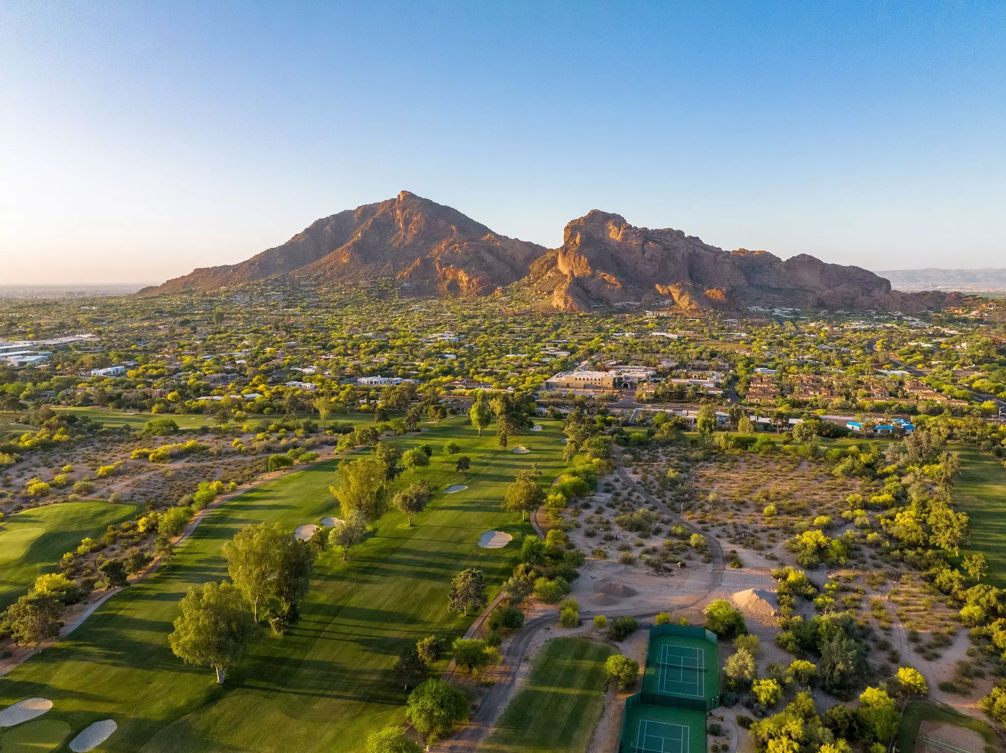 A green golf course in the foreground leads to a two-peaked rock formation in the background at sunset.