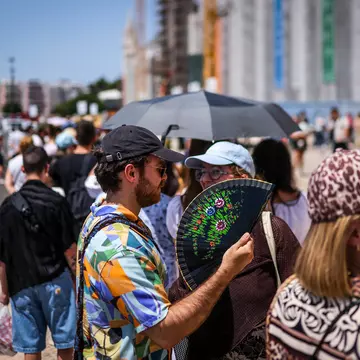 Tourists try to beat the heat with hand fans as they queue in Belém, Lisbon. 