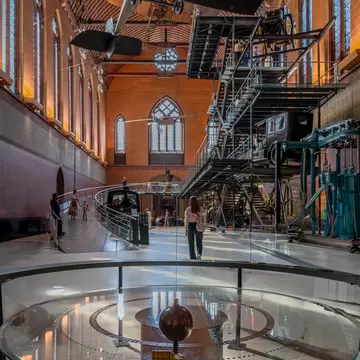 A woman walking through the Museum of Arts and Crafts with the Foucault pendulum from the church of Saint-Martin-Des-Champs in the foreground.