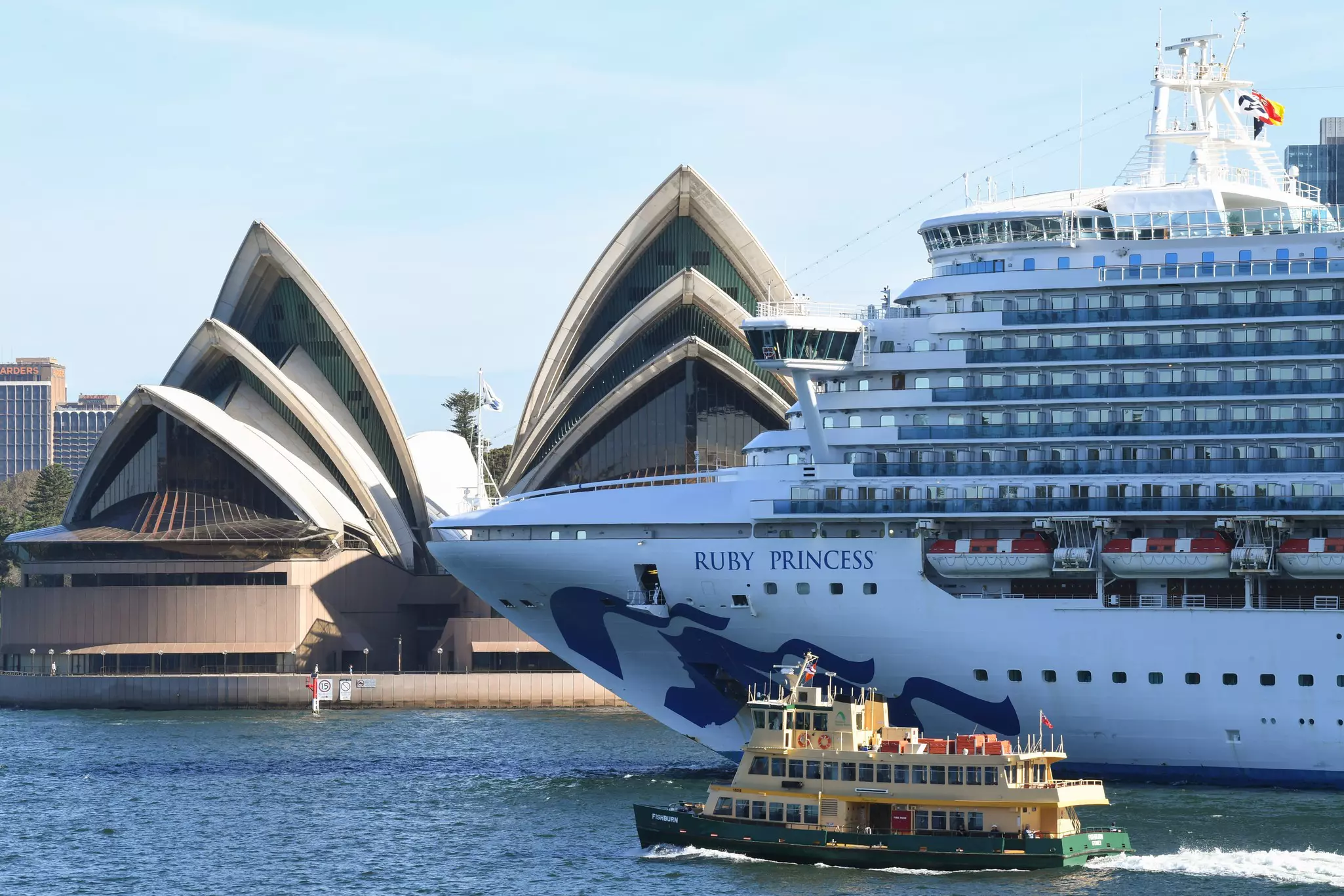 A large cruise ship passes the iconic Sydney Opera House, a building with curved sail-like architecture.