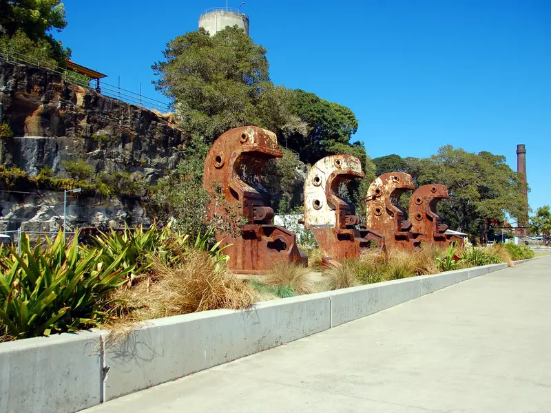 Large curved metal structures left over from industrial operations line a cement walkway on a cloudless, sunny day.
