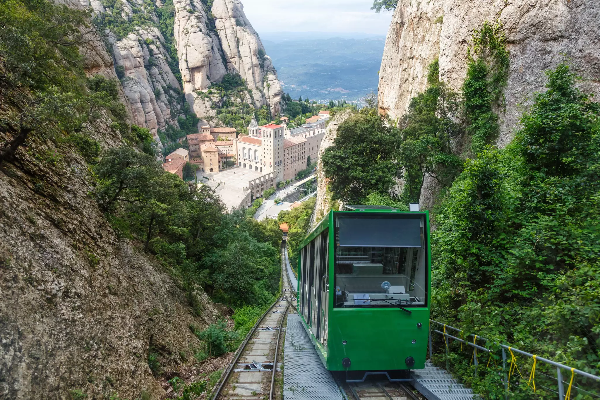 View of the green Funicular de Sant Joan cable car riding up the mountain, with the Monestir de Montserrat in the background, near Barcelona, Spain.