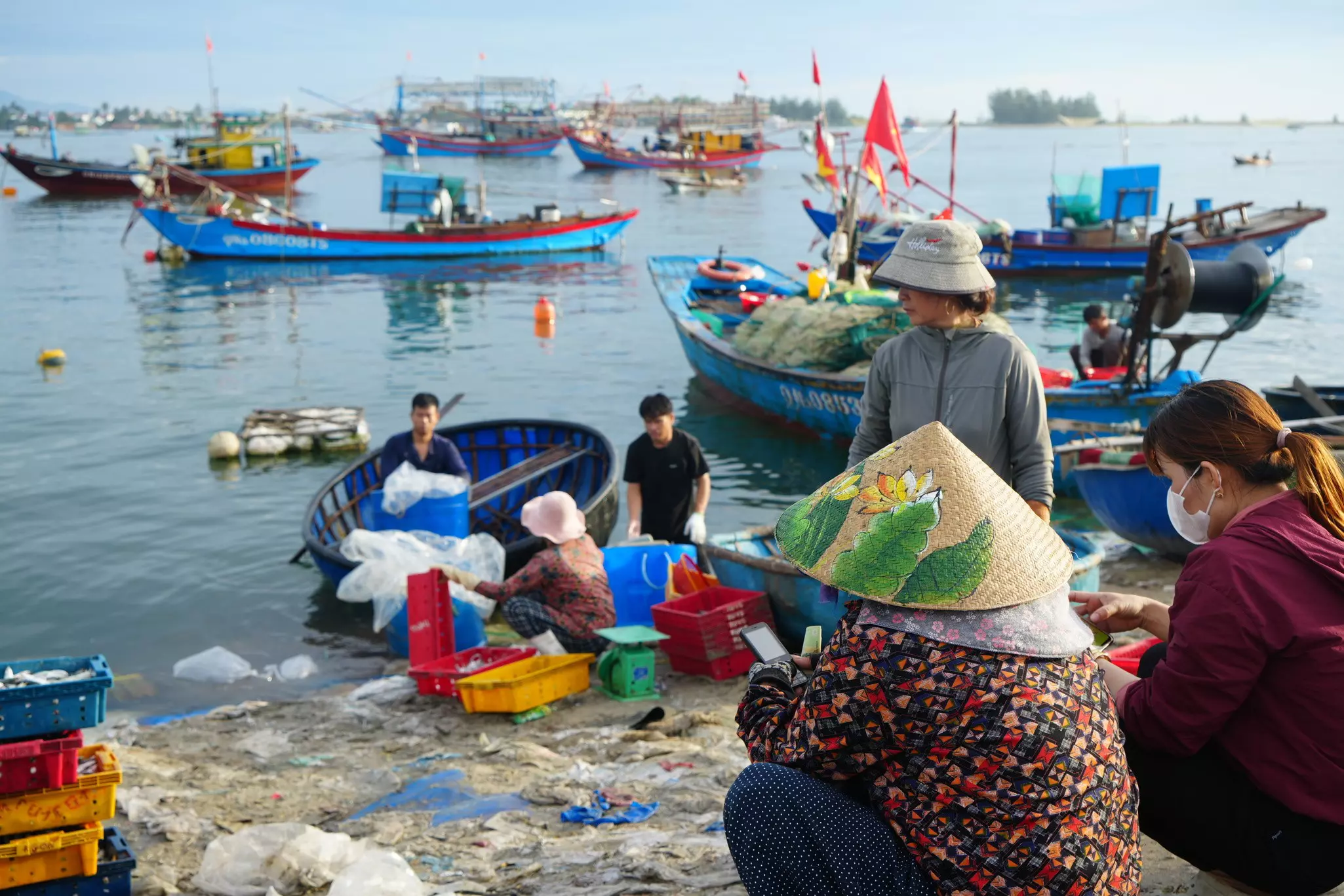 Vendors stand by a display of fresh fish on the ramp of a port. Fishing boats are seen in the water.