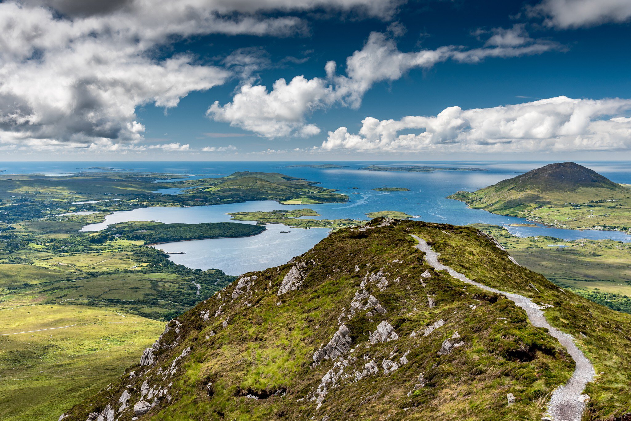 The hiking trail at the top of Diamond Hill in Connemara National Park, Ireland. Behind, the sun plays with the clouds reflected in the sea. Galway, Ireland.