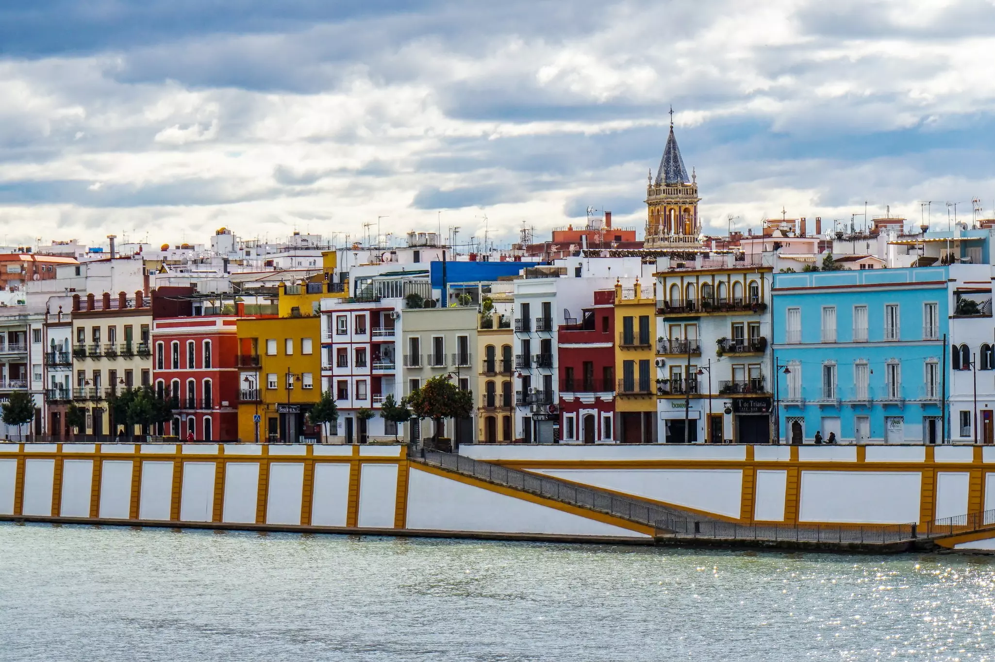 Colorful buildings sit along a street along a riverfront in a city.