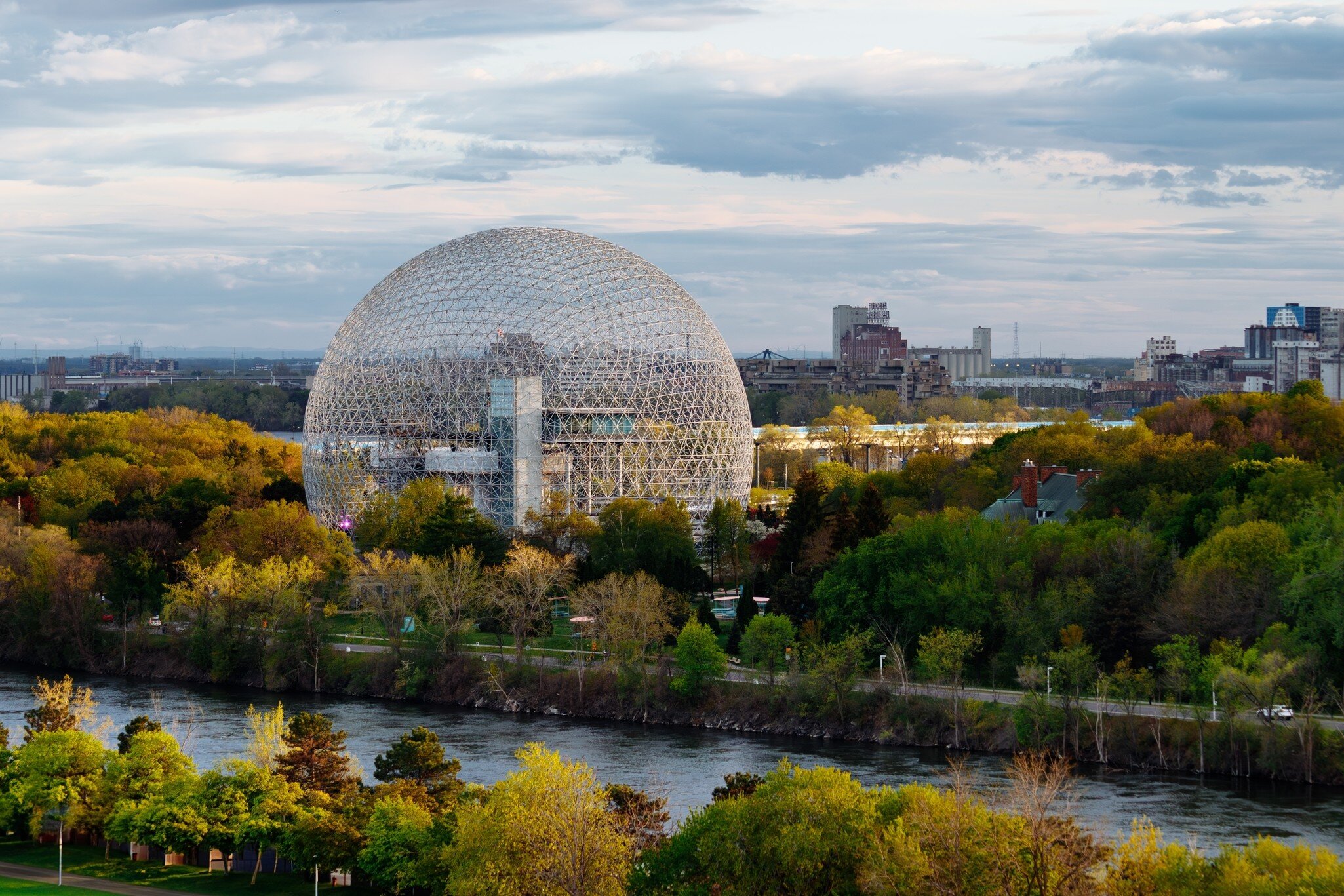 Large spherical structure surrounded by trees and a body of water 