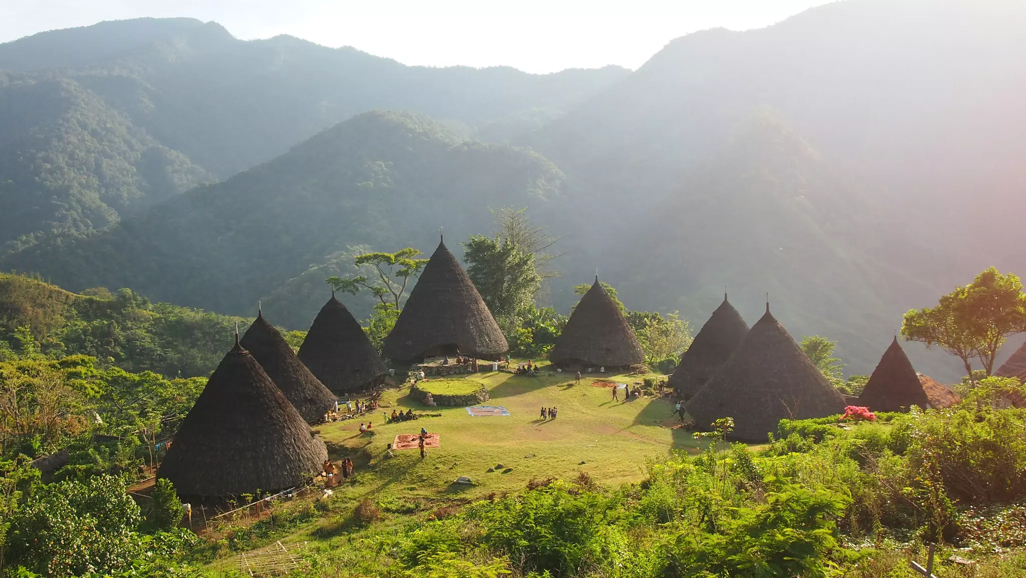 A small village with tall conical huts arranged in a circle in a lush mountain plateau.