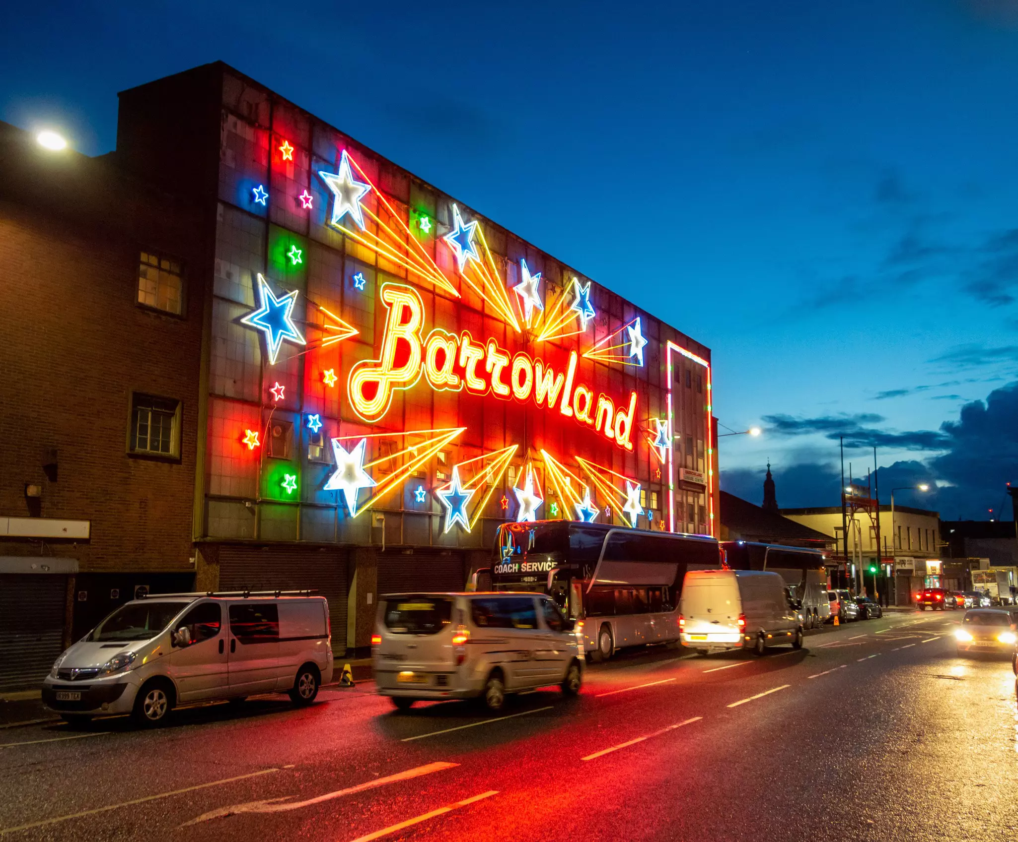 Cars drive past the illuminated facade of the Barrowland Ballroom at night in Glasgow, Scotland.