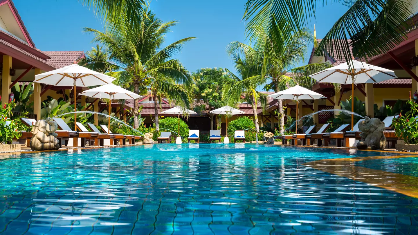 A beautiful swimming pool is surrounded by cabanas at a tropical resort.