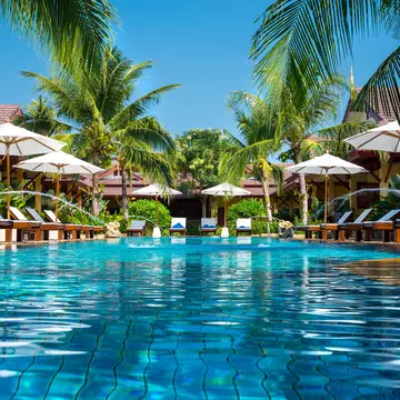 A beautiful swimming pool is surrounded by cabanas at a tropical resort.