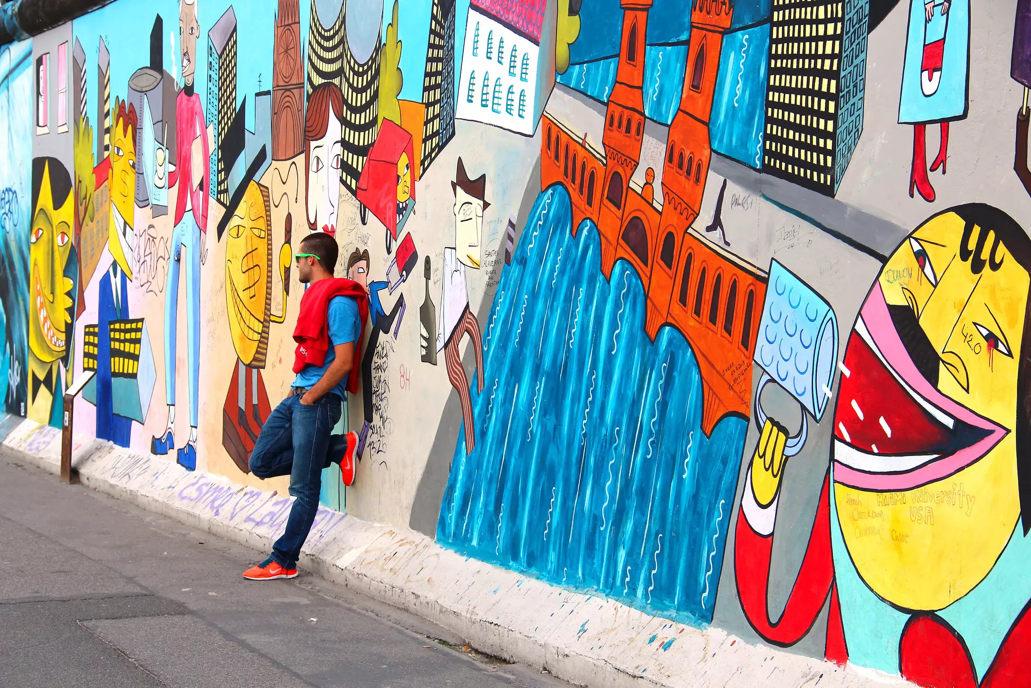 A man leans against a wall covered in red, yellow and blue graffiti