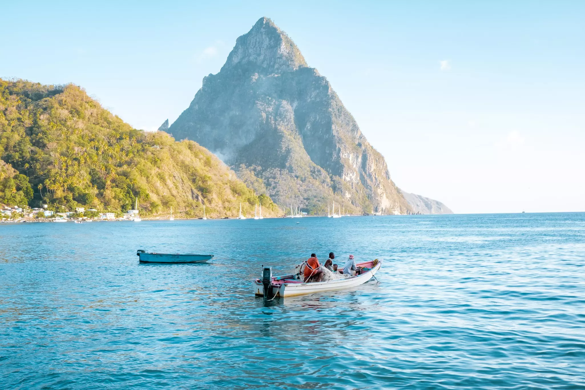 A small motorboat sails in a bay in the shadow of a pointing mountain peak.