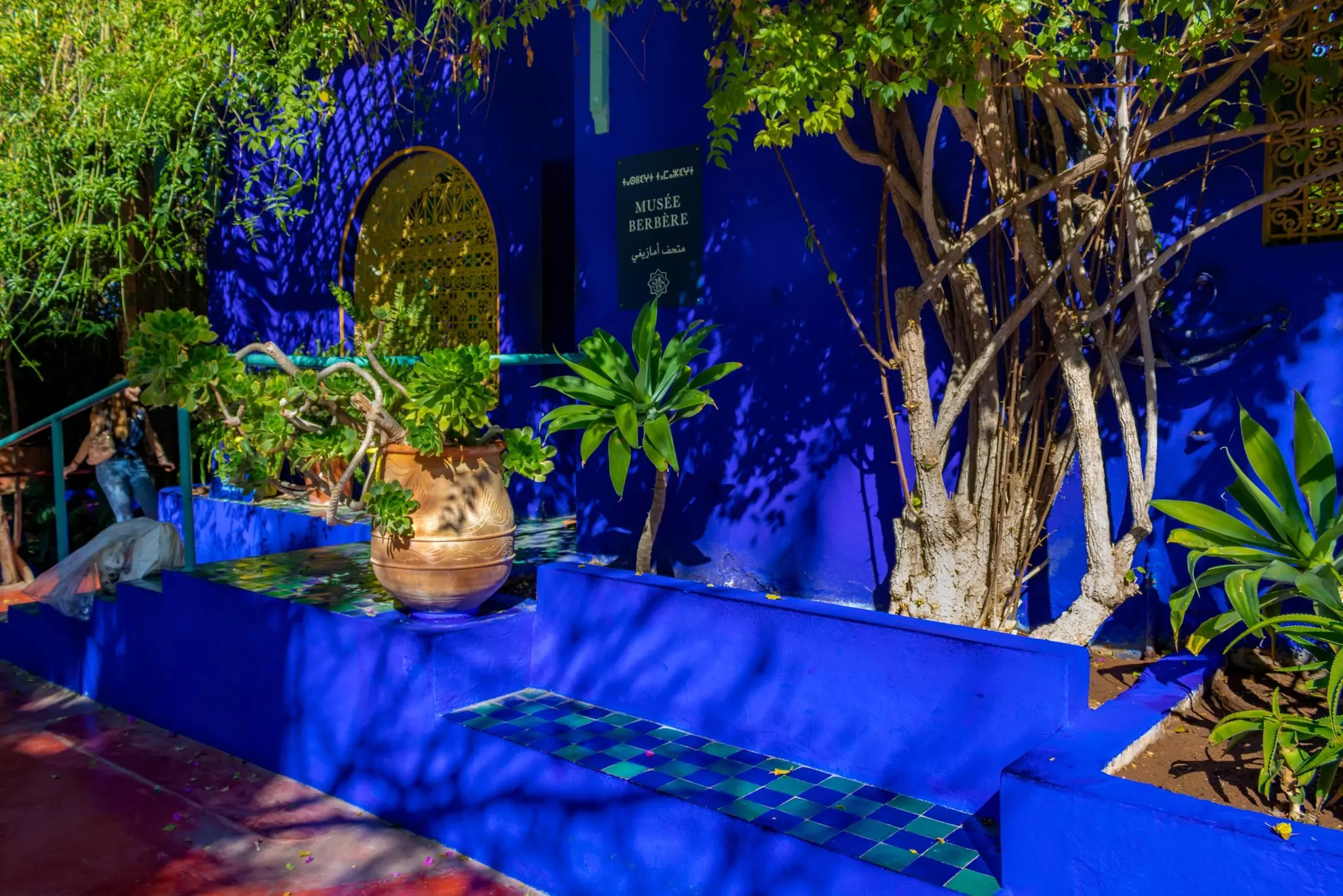 A building in a striking blue color surrounded with plants in pots has a sign that says "Musée Berbère".