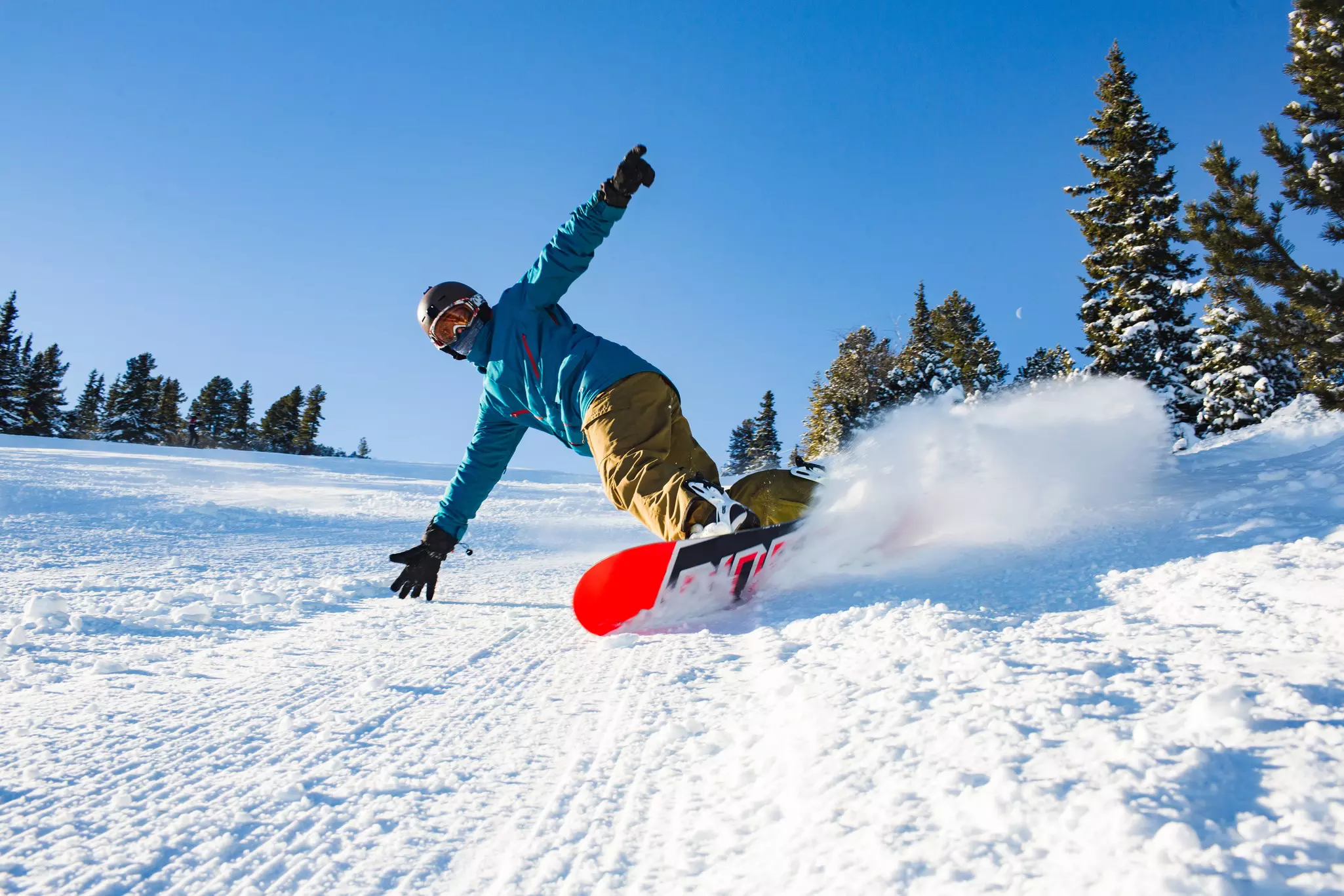 A snowboarder with arms outstretched going downhill at a sharp angle creates a spray of snow.